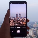 A hand holding a smartphone with Mumbai city skyline in the background, representing India smartphone market